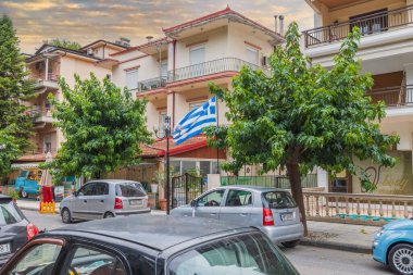 Yunanistan bayraklı güzel şehir manzarası. Açık hava restoranının yakınına park edilmiş arabalar, aydınlık yaz gününde. Yunanistan. Europa. 08.25.2021.
