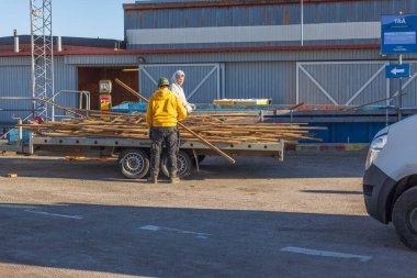 Atık geri dönüşüm istasyonunda eski tahtalarla dolu karavanı özel konteynıra boşaltan iki adamın görüntüsü. İsveçli. Enkoping. 02.20.2022.