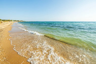 Parlak bir yaz gününde güzel bir kıyı şeridi manzarası. Kumdan kıyı şeridi ve mavi deniz suyu bulutsuz mavi gökyüzüne karışıyor. Yunanistan. 