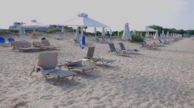 Yaz günü deniz manzarası karşısında güneşli şezlonglar ve şemsiyelerle boş kumsalın güzel manzarası. Yunanistan.