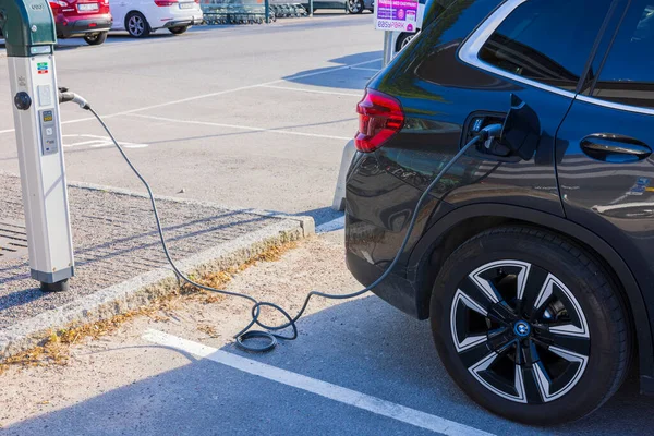 Elektrikli taşıt şarj istasyonundan siyah BMW 'ye bağlanan kabloyu kapat. İsveç. Uppsala. 05.23.2022.