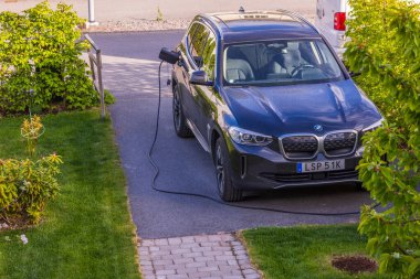 BMW ix3 elektrikli arabanın özel otoparktaki şarj kablolu görüntüsünü kapat. İsveç. Uppsala. 06.12.2022.
