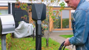 Özel otoparkta elektrikli arabanın şarj kablosunu şarj eden adamın yakın görüntüsü. İsveç.