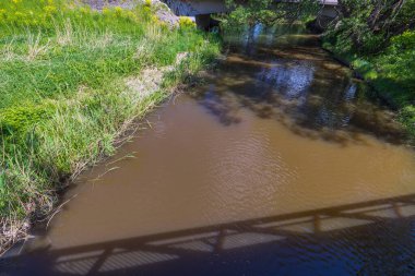 Güneşli bir yaz gününde ağaçların yansımasıyla köprüden nehre güzel bir manzara. İsveç.