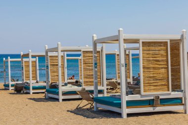 Deniz kıyısındaki güneşli sahil manzarası otel turistleri için rahat güneşli yataklar. Rodos. Yunanistan. 07.15.2022