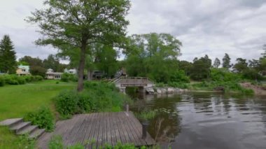 Beautiful view of architecture with villas in village on lake with bridge and forest trees. Sweden.