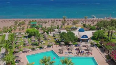 Beautiful view of hotel area with access to sandy beach with people resting on sun loungers under sun umbrellas. Rhodes. Greece. 08.06.2022.