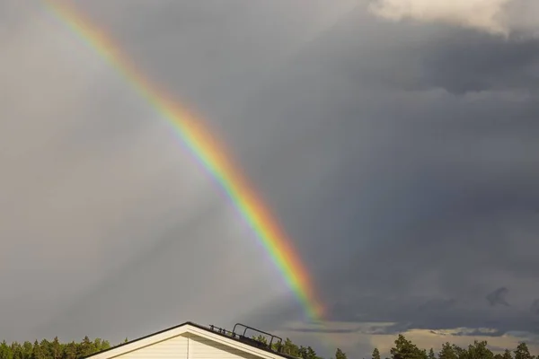 Beautiful view of rainbow after rain over roofs of pitchforks on warm summer day. Sweden.