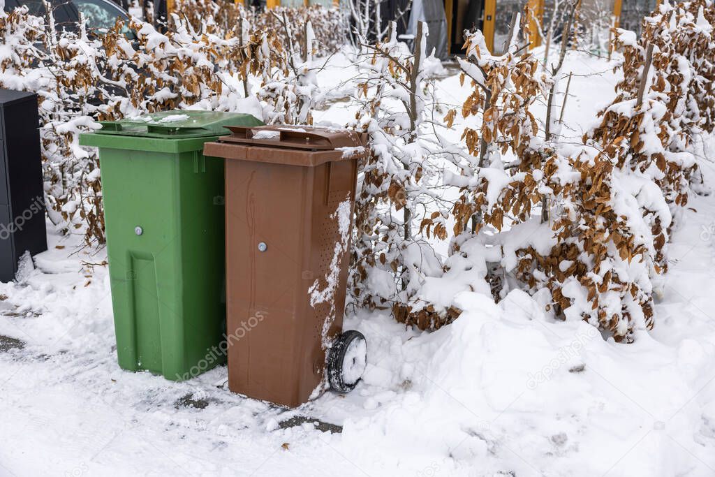 Close up view of waste and recycling containers against backdrop of snow-covered bushes in front of private villa. Sweden.