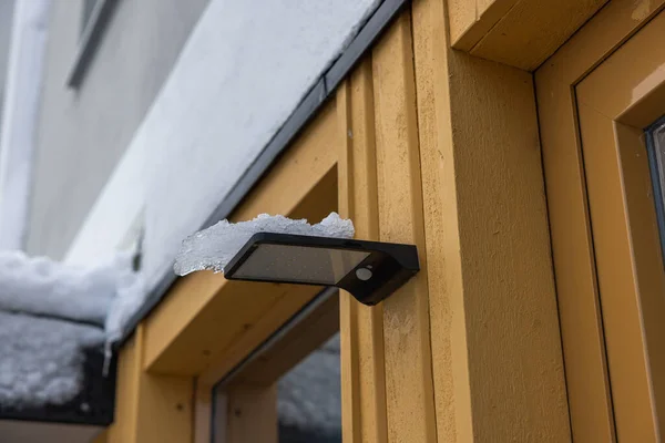 Close up view of wooden villa with outdoor lamp with solar panel and motion sensor covered in snow. Sweden.