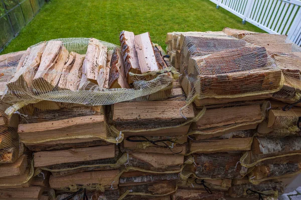 View of birch firewood in transport nets on backyard on green grass lawn background.  Sweden.