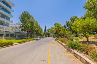 Boş asfalt yol boyunca yeşil ağaçların ve bulutsuz mavi gökyüzü arka planındaki otobüs durağının güzel manzarası. Rodos. Yunanistan. 08.23.2022.