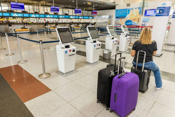 机场内妇女坐在手提包上的内景 在行李投递标志前 2022 — 图库照片