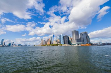 Hudson nehrinin her iki yakasındaki Manhattan gökdelenlerinin muhteşem manzarası mavi gökyüzünün altında beyaz bulutlarla. New York, ABD.