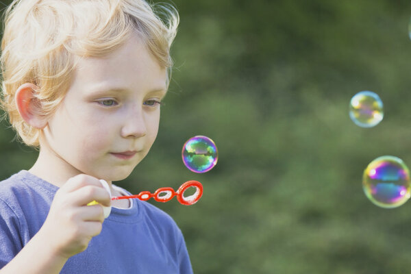 Blond boy in blue shirt blows bubbles