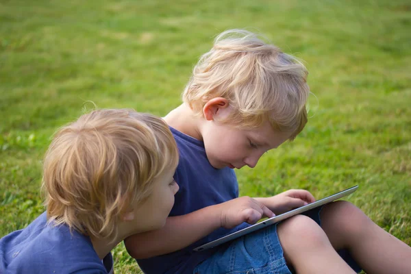 De blonde jongens zijn spelen met de tablet pc buiten. — Stockfoto