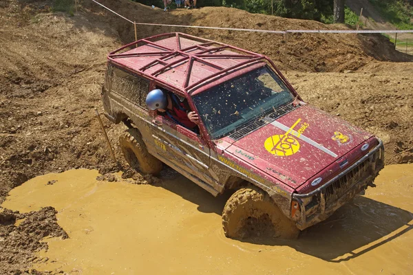 Auto rossa fuoristrada che passa in pozzanghere fangose — Foto Stock