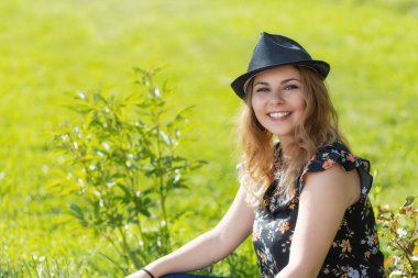 Siyah hasır şapkalı, yaz günü açık havada poz veren çekici bir kadının portresi. Yatay olarak. 