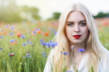 Çekici sarışın bir kadının çiçek ve haşhaş otlağındaki portresi. Yatay olarak. 