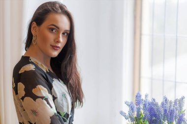 Çekici siyah saçlı kız mor çiçeklerin yanında poz veriyor. Yatay olarak. 