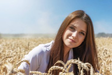 Gülümseyen esmer kadın buğday tarlasında poz veriyor. Yatay olarak.