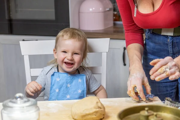 Laughing little child boy is helpful in baking cookies in the kitchen. Little helper