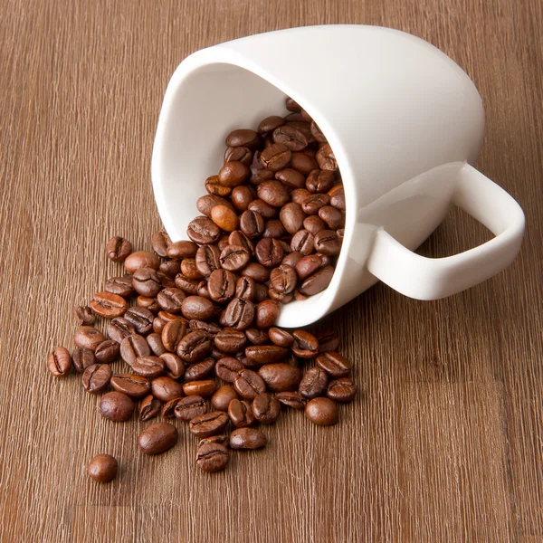 Xícara de café e grãos de café derramados — Fotografia de Stock
