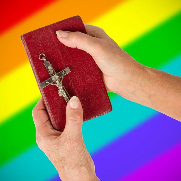 Old hands holding a very old bible, rainbow flag pattern — Stock Photo, Image