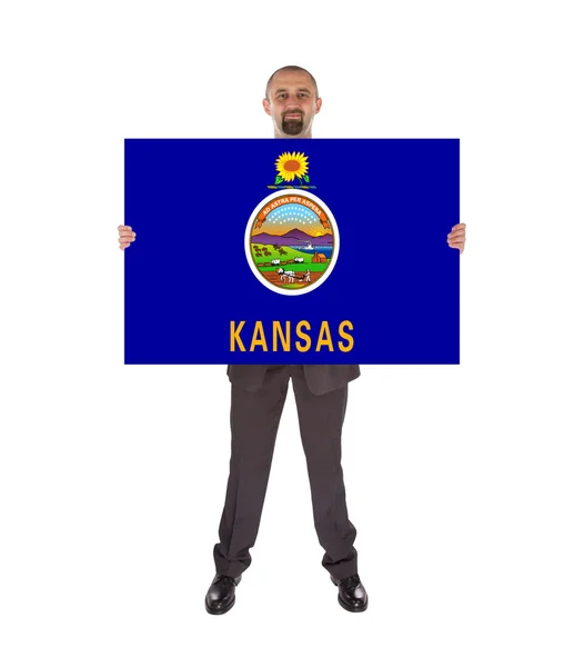 Un hombre de negocios sonriente sosteniendo una tarjeta grande, bandera de Kansas — Foto de Stock