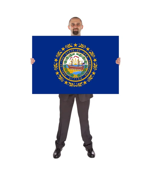 Un hombre de negocios sonriente sosteniendo una tarjeta grande, bandera de New Hampshire — Foto de Stock