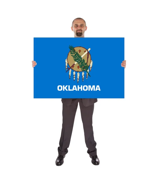 オクラホマ州の旗の大きなカードを保持しているビジネスマンの笑みを浮かべてください。 — ストック写真