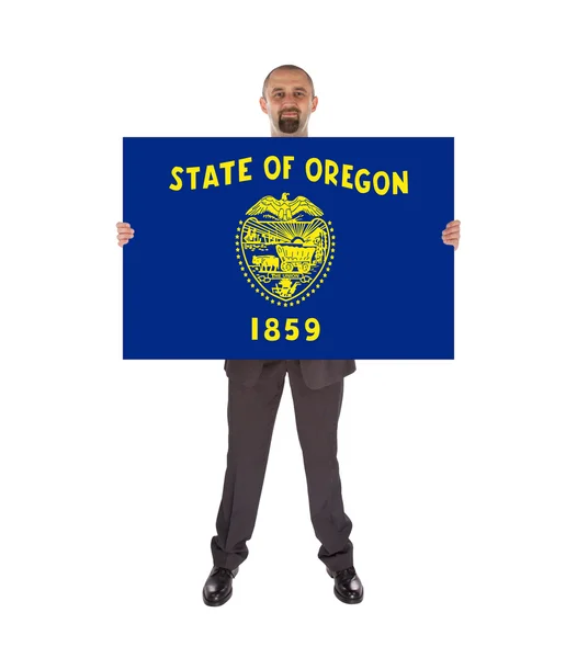 Un hombre de negocios sonriente sosteniendo una tarjeta grande, bandera de Oregon — Foto de Stock