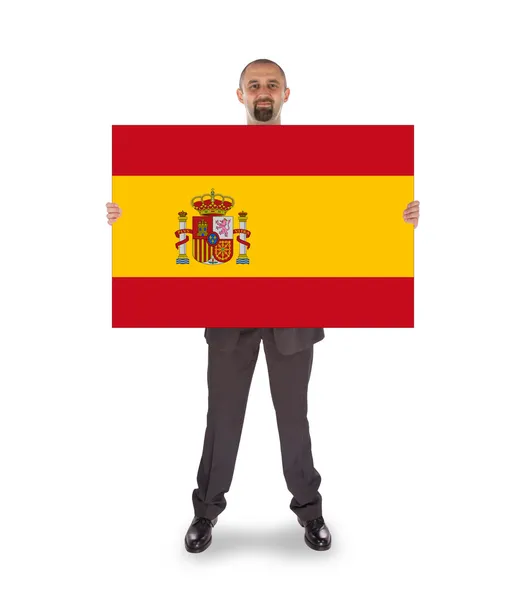 Un hombre de negocios sonriente sosteniendo una tarjeta grande, bandera de España — Foto de Stock