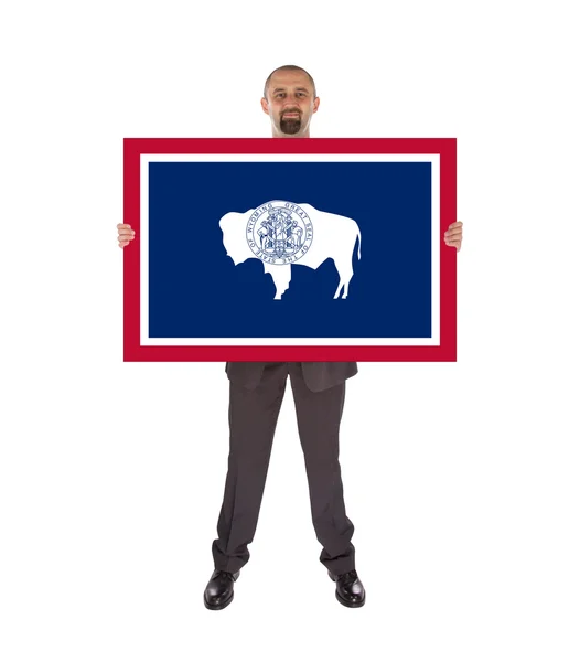 Un hombre de negocios sonriente sosteniendo una tarjeta grande, bandera de Wyoming — Foto de Stock