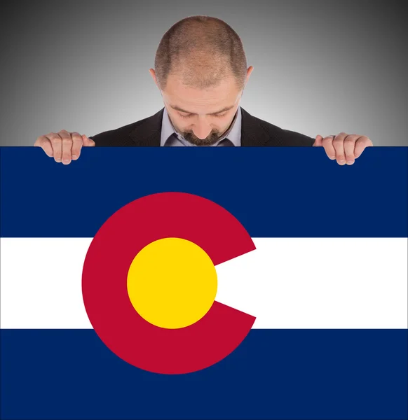コロラド州の旗の大きなカードを保持しているビジネスマンの笑みを浮かべてください。 — ストック写真