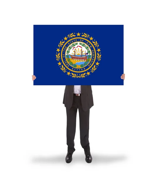 Un hombre de negocios sonriente sosteniendo una tarjeta grande, bandera de New Hampshire — Foto de Stock