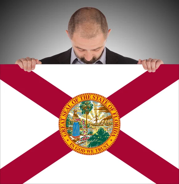Hombre de negocios sonriente sosteniendo una tarjeta grande, bandera de Florida — Foto de Stock