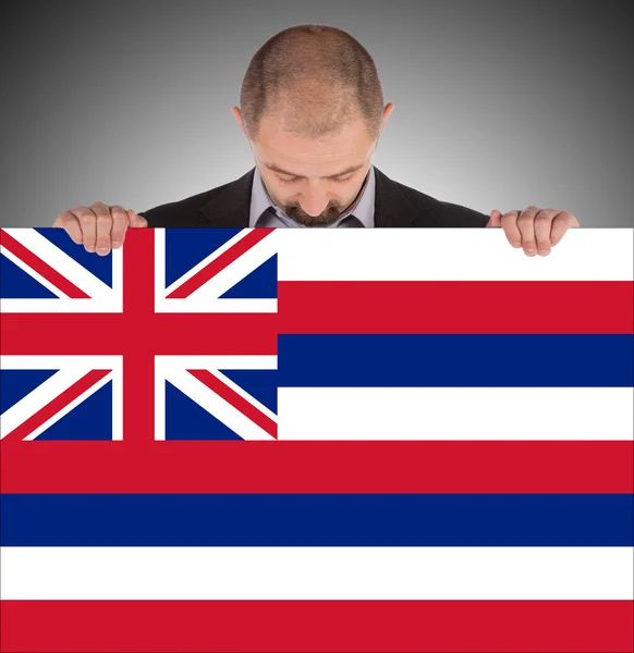 Un hombre de negocios sonriente sosteniendo una tarjeta grande, bandera de Hawaii —  Fotos de Stock