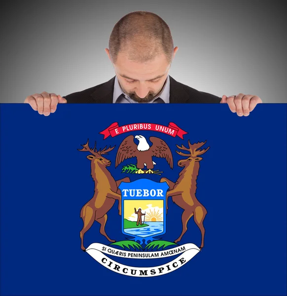 Leende affärsman håller ett stort kort, flagga michigan — Stockfoto