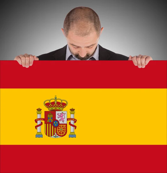 Un hombre de negocios sonriente sosteniendo una tarjeta grande, bandera de España —  Fotos de Stock