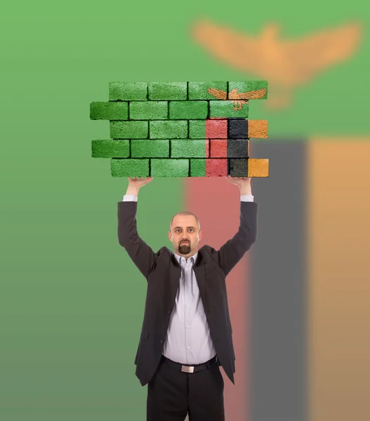 Empresário segurando um grande pedaço de uma parede de tijolo — Fotografia de Stock