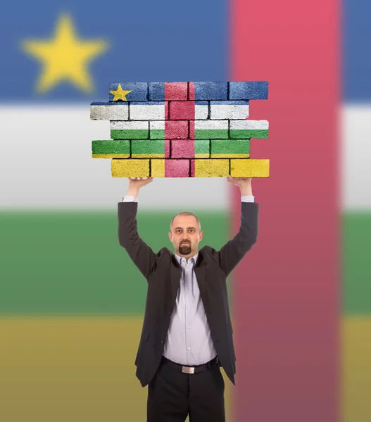 Businessman holding a large piece of a brick wall — Stock Photo, Image