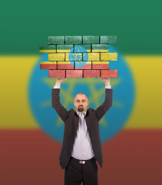 Businessman holding a large piece of a brick wall — Stock Photo, Image