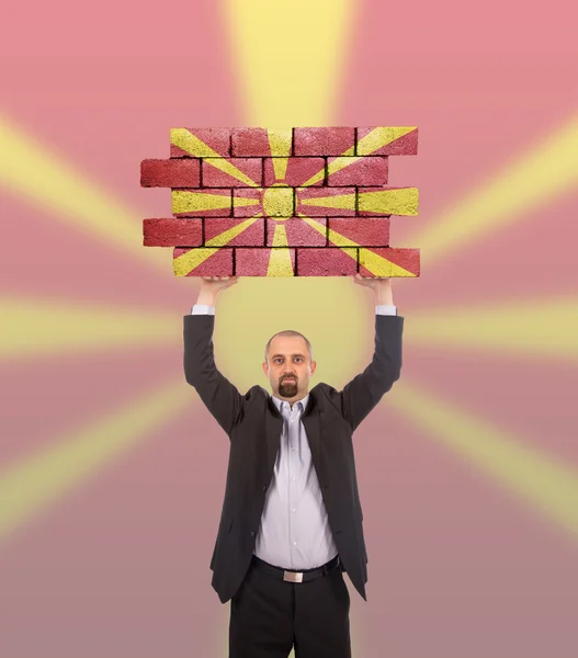 Businessman holding a large piece of a brick wall — Stock Photo, Image