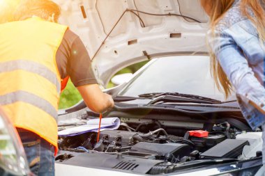 Motorlu taşıt tamircisinin güneş ve mercek flaşlı tamir geçmişini kaydetmek için motor yağını kontrol etmesi ve kapatması.