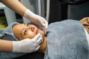 Kozmetik uzmanı, güzellik kliniğindeki kadın müşterinin yüzünü temizlemek için pamuk pedi kullanıyor..