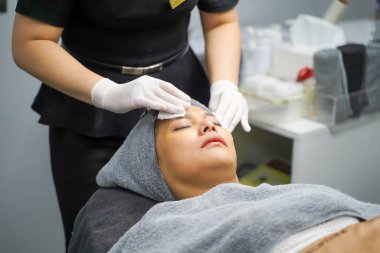 Kozmetik uzmanı, güzellik kliniğindeki kadın müşterinin yüzünü temizlemek için pamuk pedi kullanıyor..