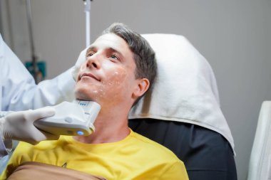 Yakından yakışıklı bir adam profesyonel kozmetik uzmanının cildini canlandırmak için renkli ışık terapisi görüyor..