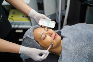 Kapalı kozmetik uzmanı güzellik kliniğinde kadın hasta yüzüne yüz jölesi sürmek için kozmetik fırçası kullanıyor..