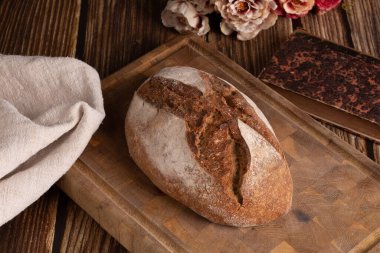 Rustic bread on a cutting board with flowers on a wooden table